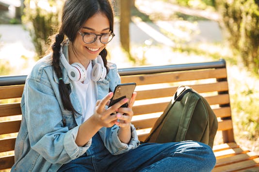 Girl sitting on a park bench looking at her phone