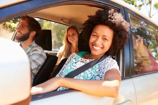 Young girl leaning her head out the car window and smiling, she just got her drivers license through Aceable