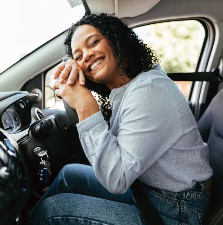 Smiling girl seated in the driver's seat, hugging the steering wheel