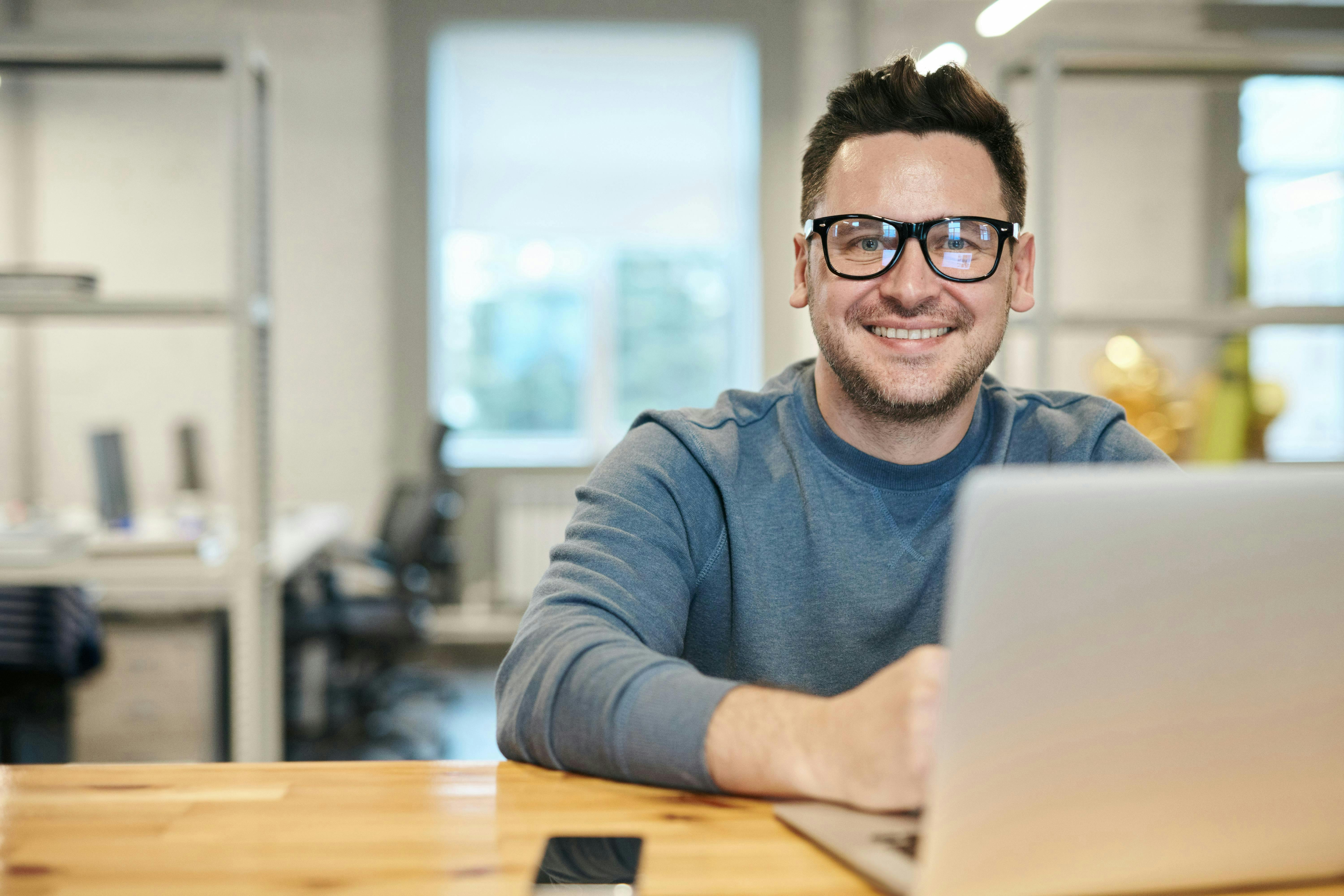 Man with glasses smiling with a computer