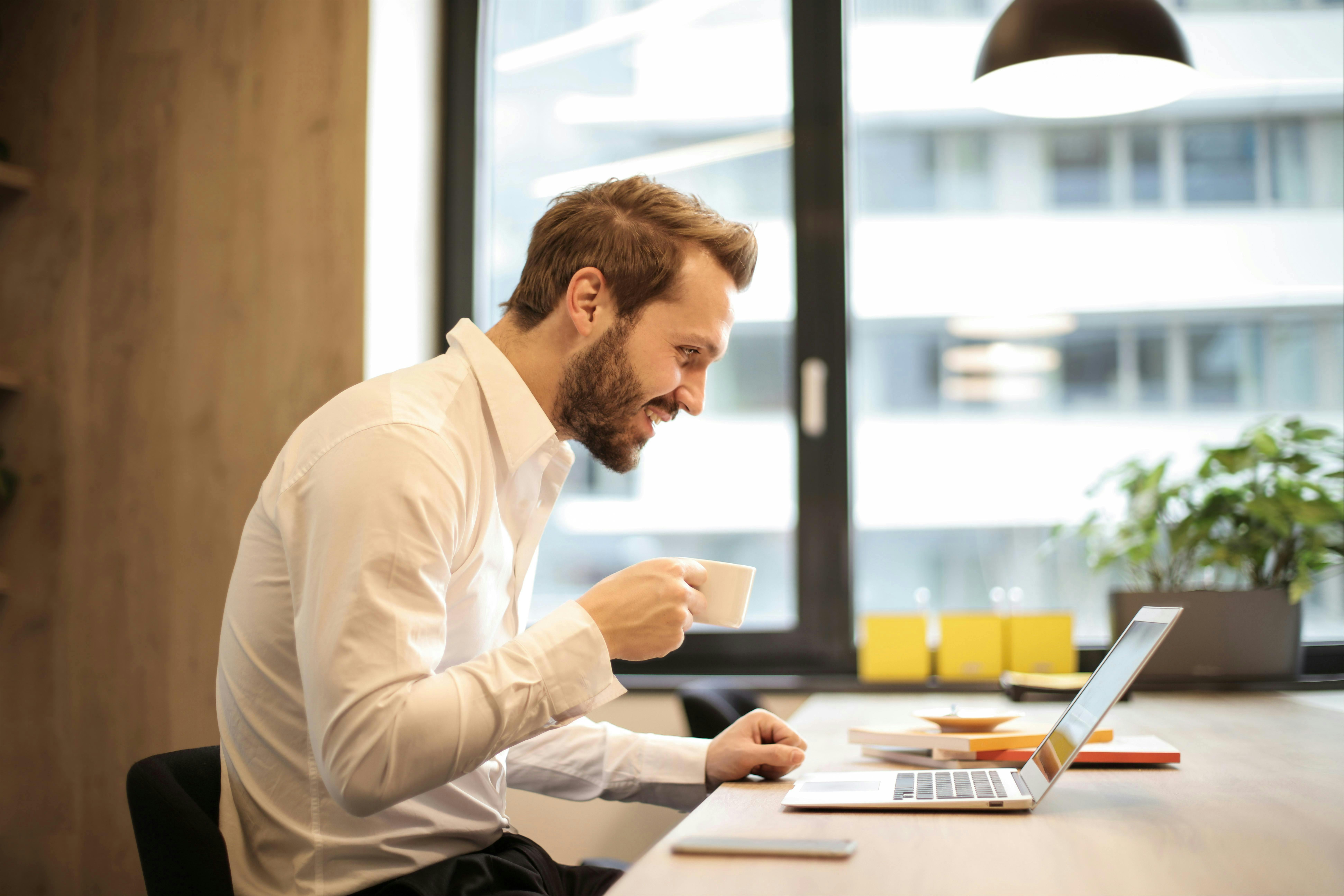Man smiling drinking coffee looking at computer