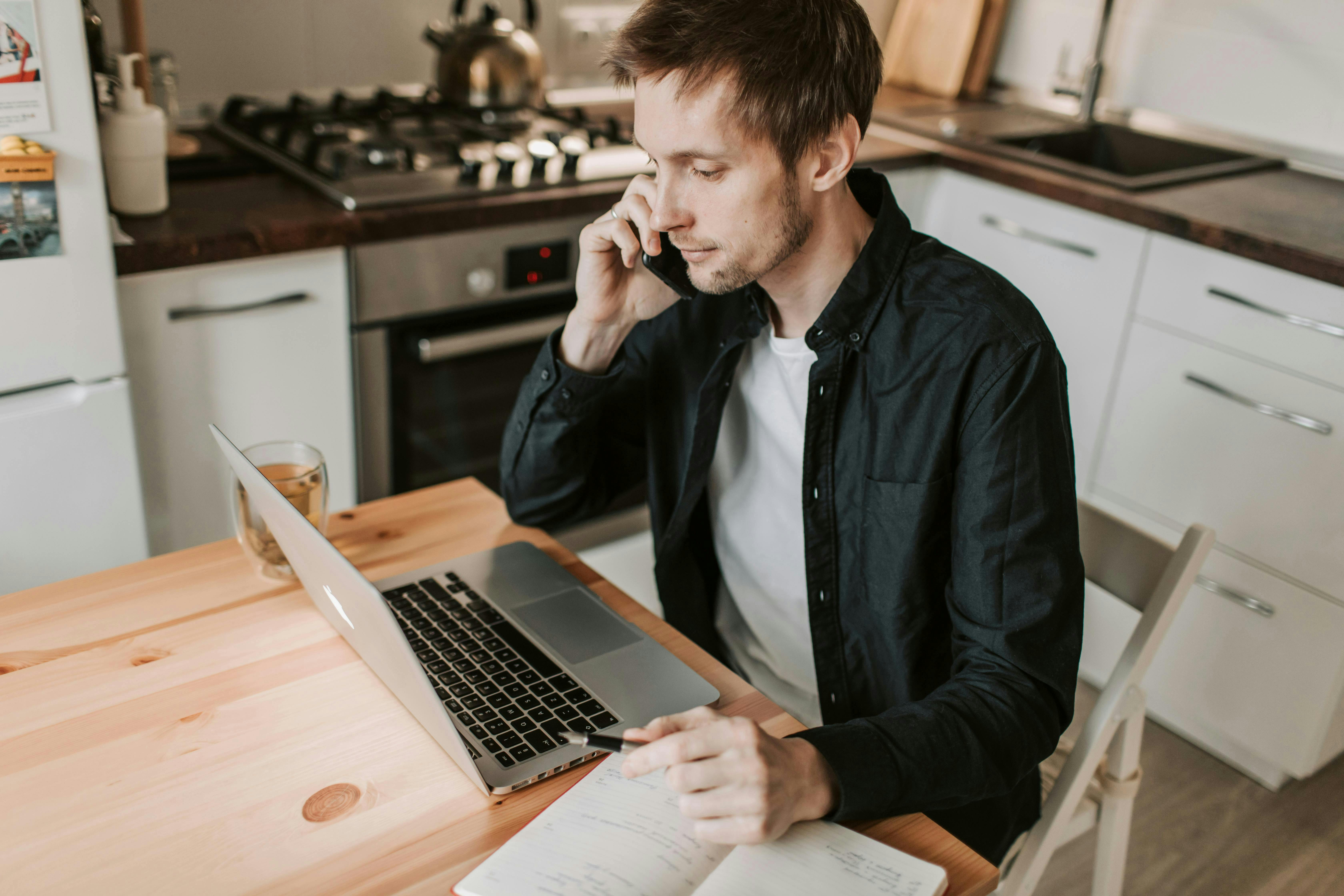 man on phone with laptop in kitchen